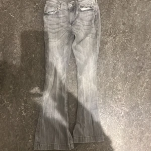 Grå flared jeans från H&M - Snygga grå jeans från H&M med flared ben och justerbar midja. De har en midwaist passform och klassiska femficksdetaljer. Perfekta för en trendig look!