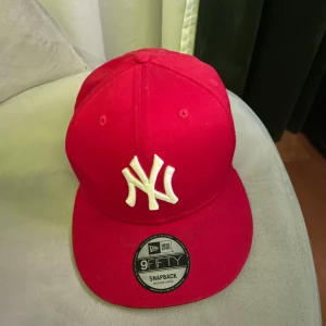 (Röd keps från New era) använd några få gånger under sommaren. Köpt för 499 kr kommer inte riktigt ihåg vart jag köpte den. STORLEK=JUSTERBAR(PRISET KAN DISKUTERAS VID SNABB AFFÄR)  - Snygg röd keps från New Era med vit broderad logga framtill. Kepsen har en justerbar snapback-stängning för perfekt passform. Perfekt för att ge din outfit en sportig touch.