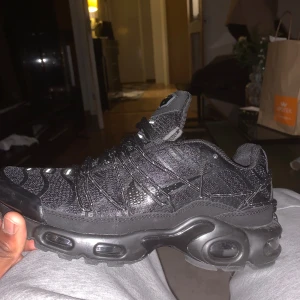 Svarta Nike sneakers - Snygga svarta Nike sneakers med en robust design och synliga luftkuddar i sulan. Skorna har en stilren svart färg med matchande snörning och en diskret Nike-logga på plösen. Perfekta för en sportig look. Storlek 41, men passar 41/2 och storlek 42. Skorna är använda Ca 4 gånger men 2 av de extra snören är sönder men de spelar ingen roll för de går att ta bort. Skorna går att göra till vanliga Nike Tn, coolt Ellerhur🤩 .Ny pris 2500, Pris kan diskuteras vid snabb affär🤩