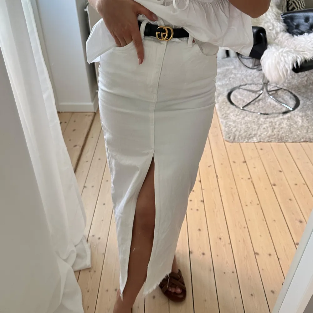 Snygg vit jeanskjol med hög midja och en stilren slits framtill. Kjolen har en klassisk femficksdesign och är perfekt för en trendig look. Den är lång och ger en elegant siluett. Finns en fläck där bak se bild . Hameet.