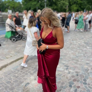 Balklänning - Elegant vinröd långklänning med smala axelband och djup urringning. Klänningen har en figurnära passform med släp. Använd en gång