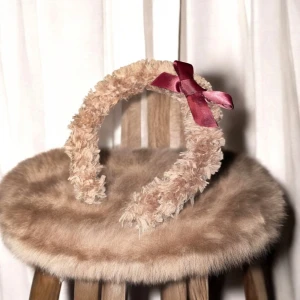 Beige fluffigt diadem med rosett - Säljer ett supergulligt beige diadem med fluffig textur och en söt vinröd rosett på sidan. Perfekt för att ge en extra touch till din outfit!