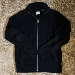 Kofta från Jack & Jones - Säljer en stilren mörkblå kofta  från Jack & Jones. Tröjan har en dragkedja framtill och långa ärmar, perfekt för kyligare dagar. Den är i storlek M och passar bra till både jeans och chinos. Han på bilden är 187 cm lång. Hör av dig vid fler funderingar 