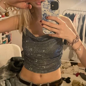 Glittrig blå/grå topp - Helt ny med lapp kvar🙌🤗Säljer en snygg glittrig blå / grå topp med smala axelband och en draperad halsringning. Perfekt för en kväll ute eller en festlig tillställning. Toppen är figurnära och ger en stilren look.