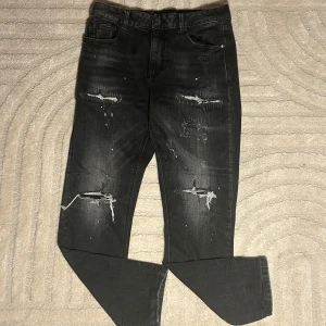 Svarta jeansbyxor från Supply & Demand - Snygga svarta jeansbyxor från Supply & Demand med slitna detaljer och en cool, distressed look. Perfekta för en avslappnad stil. Midjan är midwaist och byxorna har en straight passform.