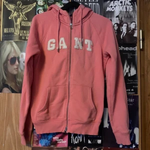 Rosa hoodie från GANT - Säljer en snygg rosa hoodie från GANT med dragkedja och stora bokstäver på bröstet. Tröjan har långa ärmar och en bekväm passform. Perfekt för en avslappnad stil.