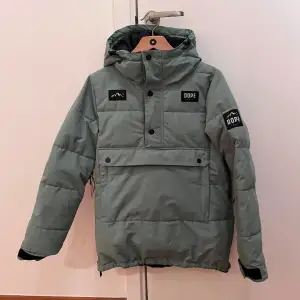 Säljer en grön pufferjacka från Dope med huva. Jackan har en stor ficka framtill, ficka för liftkort på ärmen. Perfekt för kyliga dagar. Den har långa ärmar och en stilren design. Vattentät 15.000 mm DRY tech. Väldigt fint skick. Använd 2,5 skidveckor. Från djur- och rökfritt hem. Nypris 2199:- 