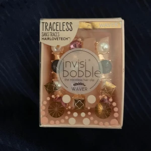 Hårklämmor från Invisibobble - Säljer ett set med tre eleganta hårklämmor från Invisibobble. Klämmorna har en guldig bas med dekorativa pärlor och stenar i rosa, lila och svart. Perfekta för att ge en stilfull touch till din frisyr.