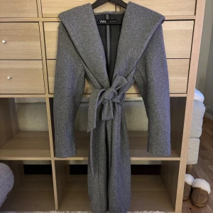 Grå kappa från Zara - En grå kappa från Zara med knytband i midjan. Kappan har använts maximalt två gånger och är i mycket bra skick.