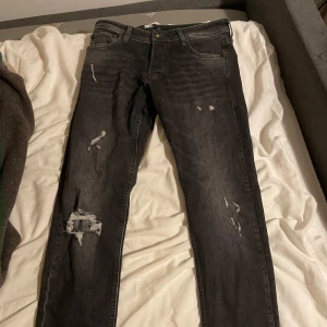 Svarta jeans från Jack & Jones Sprillans ny slim fit - Snygga svarta jeans från Jack & Jones med slitna detaljer för en trendig look. De har en klassisk femficksdesign och en bekväm passform. Perfekta för en avslappnad stil.