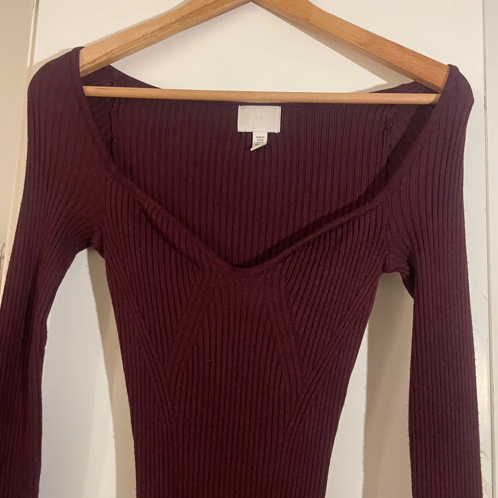 Snygg vinröd ribbad klänning från H&M med lång ärm och v-ringad design. Perfekt för en stilren look. Klänningen är figurnära och har en elegant passform som framhäver silhuetten.. Mekot.