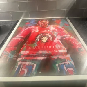Limiterad hockey tavla 50 x 70  - Säljer en färgglad tavla med motiv av en den legendariska hockey spelaren joel lundqvist röd tröja med texten 'SILVERBULLET'. Tavlan har en vit eklusiv ram med måtten 50 x 70 och konstverket är fyllt med livliga färger som blått, grönt och rosa. Den är signerad av joel lundqvist. Perfekt för sportentusiaster och konstälskare!
