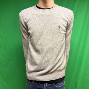 Grå merino ull tröja från Ralph Lauren - Säljer en stilren grå tröja från Ralph Lauren med en vinröd logga broderad på bröstet. Tröjan har långa ärmar och svarta armbågslappar som ger en snygg detalj. Perfekt för en avslappnad men ändå elegant look. Storlek S men modellen är M då kan passa på M också. Fråga gärna frågor om modellens mått och så vidare. Pris kan diskuteras vid snabb affär.😄