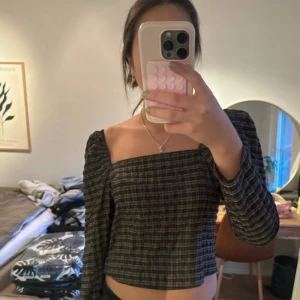 Rutig offshoulder topp - Säljer en superfin rutig offshoulder topp i mörka toner. Den är croppad och har långa ärmar, perfekt för en stilren look. Toppen är i bra skick och passar perfekt till både vardag och fest. Skicka ett meddelande vid intresse!