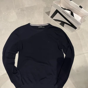 Mörkblå tröja från J.Lindeberg - Säljer en stilren mörkblå tröja från J.Lindeberg. Tröjan har en klassisk design med rund hals och långa ärmar. Perfekt för en elegant och avslappnad look. Köpt på NK men nästan aldrig använd - kvitto finns givetvis! Hör av dig vid frågor eller intresse!