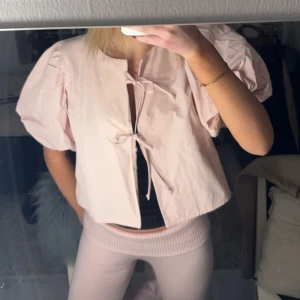 Ljusrosa blus med puffärmar - Säljer en söt ljusrosa blus med puffiga kortärmar och knytning framtill. Perfekt för en trendig look.