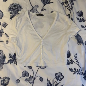 Vit croppad topp med knappar - Säljer en vit croppad topp från shein med v-ringning och knappar framtill. Perfekt för en avslappnad stil. Toppen har korta ärmar och är gjord i ett mjukt bomullsmaterial.