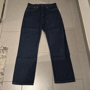 Levi's jeans i mörkblå denim - Snygga Levi's jeans i mörkblå denim med klassisk femficksdesign och knappgylf. Perfekta för en avslappnad stil. Märkeslappen baktill ger en autentisk touch.
