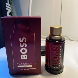Boss The Scent Elixir Parfum Intense - Säljer en elegant och förförisk parfym från Hugo Boss, The Scent Elixir. Flaskan är i en djup röd färg med guldlock och rymmer 50 ml. Doften är en rik blandning av röd pimento, caledonisk sandelträ och lavandin absolut, vilket ger en intensiv och lockande upplevelse. Parfymen säljs pga att sig på något nytt. Den är endast testad med ett sprut vilket betyder nyskick. Box ingår vid köp.