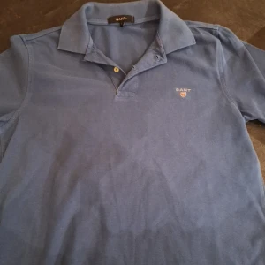Blå pikétröja från GANT - Säljer en klassisk blå pikétröja från GANT med korta ärmar och en liten broderad logotyp på bröstet. Är L men passar M.