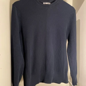 Mörkblå stickad tröja från Zara - Säljer en stilren mörkblå stickad tröja från Zara. Tröjan har en klassisk rund hals och långa ärmar, perfekt för kyligare dagar. Den har en ribbad struktur som ger en snygg och tidlös look.