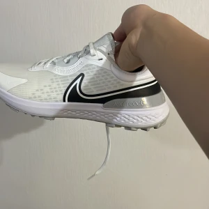 Vita Nike React sneakers - Säljer ett par vita Nike React sneakers med svart swoosh och grå detaljer. Skorna har en modern design med snörning och är perfekta för träning eller vardagsbruk. De är tillverkade i syntetmaterial för en lätt och bekväm känsla.  Nike Infinity PRO 2 . Storlek 43