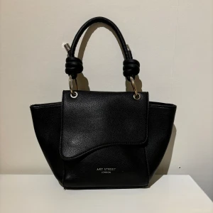 Svart handväska  - Snygg svart handväska från Art Street London. Två innerfickor, en av dem med dragkedja och en ficka på utsidan med dragkedja. Säljer då jag inte använder den. Pris kan diskuteras vid snabb affär.