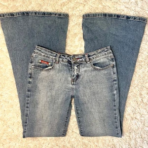 Blå lågmidjade bootcut jeans med broderade detaljer - Snygga blå lågmidjade bootcut jeans från Venus Ross med unika broderade detaljer på bakfickorna. Avklippta längst ner så de passar någon som är ca 167! Midjemått 38 cm