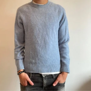 Uniqlo Ulltröja  - Säljer en stilren ljusblå tröja från Uniqlo. Tröjan är tillverkad i ett mjukt material och har en klassisk rund halsringning. Perfekt för en avslappnad look.