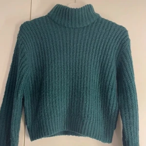 Grön stickad polotröja - Säljer en mysig grön stickad polotröja med ribbad struktur. Tröjan har långa ärmar och en croppad passform som ger en modern look. Perfekt för kyliga dagar.