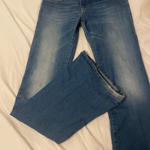 Blå Lågmidjade bootcut jeans från Diesel - Snygga blå jeans från Diesel med klassisk femficksdesign och märkets logga på den lilla fickan. Jeansen har en bootcut passform och är tillverkade i slitstarkt denim. Perfekta för en avslappnad stil. Midja- 34 innerbenslängd- 85 midjehöjd- 18