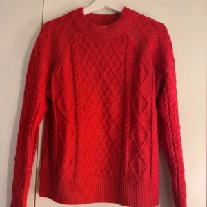 Röd stickad tröja - Säljer en snygg röd stickad tröja med ett klassiskt flätmönster. Tröjan har långa ärmar och en rund halsringning, perfekt för kyligare dagar. Passar utmärkt till både vardag och speciella tillfällen.