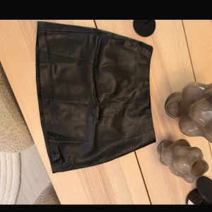 Svart skinnkjol från pull&bear” Aldrig använt ” - Snygg svart skinnkjol från pull&bear i kort modell. Perfekt för att ge en edgy touch till din outfit. Kjolen har en stilren design utan extra detaljer, vilket gör den lätt att matcha med olika toppar och accessoarer.