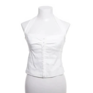 Vit halterneck korsett - Snygg vit halterneck korsett med knäppning fram. Perfekt för en stilren look. Passar bra till både jeans och kjol.