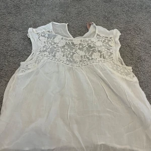 Vit ärmlös blus från KappAhl - Säljer en söt vit blus från KappAhl i storlek 40. Den är ärmlös och har vackra spetsdetaljer upptill. Perfekt för sommardagar eller en avslappnad vårlook. Blusen är i bra skick och redo för en ny ägare!
