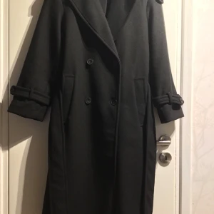 Svart vinterkappa Bershka XS. - Helt ny vinterkappa från Bershka! Köpt från nätbutiken i år. Jag har klippt bort prislapparna men kappan är aldrig använd, endast provad inomhus. Total längd: ca 109 cm Axelbredd: ca 45 cm Bröstbredd: ca 45 cm Ärmlängd: ca 55 cm. 22%ull 