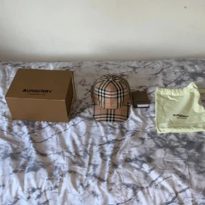 Rutig keps från Burberry - Säljer en snygg rutig keps från Burberry i klassiskt beige, svart och rött mönster. Kepsen är i nyskick och kommer med originalförpackning och dustbag. Perfekt för att ge din outfit en lyxig touch! 🧢Kvitto finns i mobilen för bevis