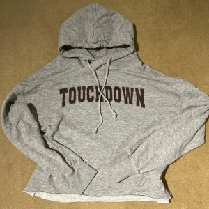 Grå hoodie från Lager 175 - Säljer en grå hoodie från Lager 175 med texten 'TOUCHDOWN' i svart och orange på bröstet. Den är supermjuk och perfekt för en chill dag. Har en klassisk känguruficka och justerbar huva. Perfekt för höst och vår!