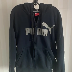 Marinblå hoodie från Puma - Säljer en marinblå  hoodie från Puma i storlek L. Den har en dragkedja framtill och en stor Puma-logga på bröstet. Perfekt för en avslappnad stil eller träning. Den är i bra skick och superbekväm att ha på sig. Hör av dig om du är intresserad!Nyskick!