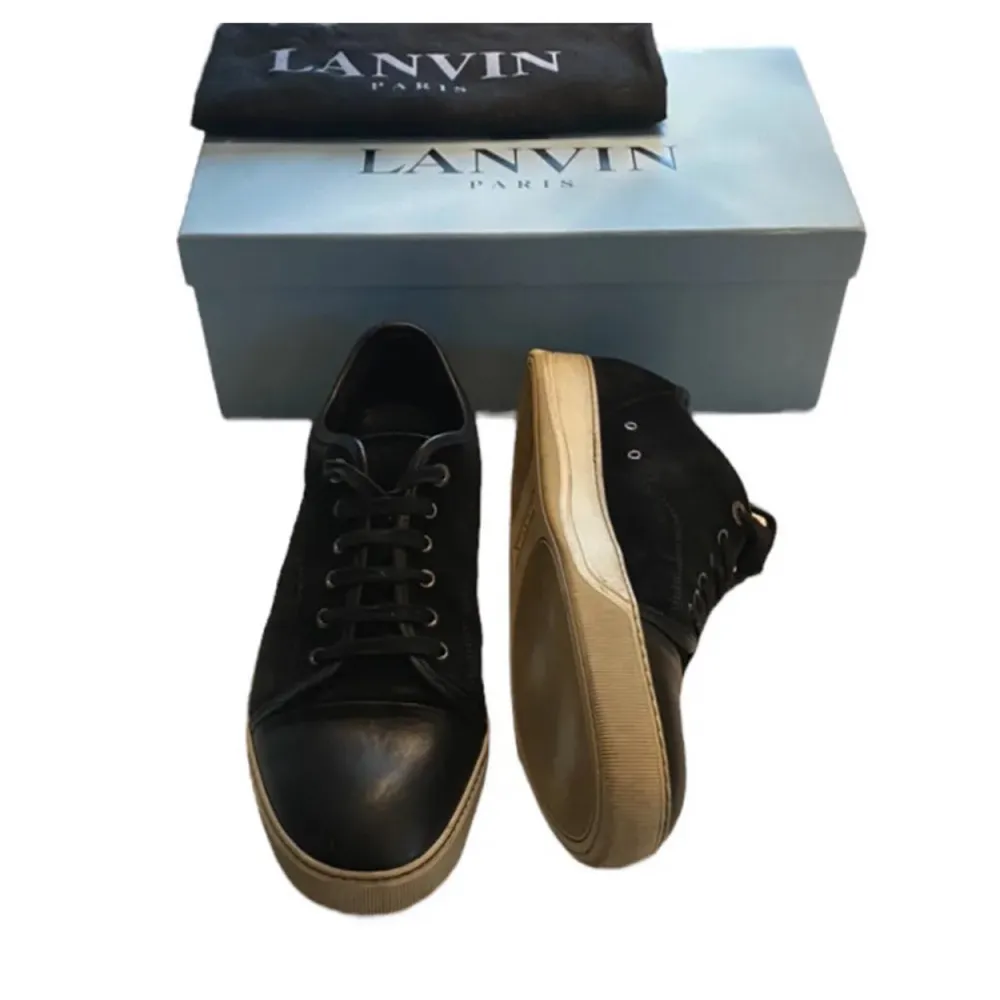 Säljer ett par stilrena svarta sneakers från Lanvin. De har en snygg kombination av mocka och skinn med klassisk snörning. Sulan är i en kontrasterande beige färg som ger en cool look. Perfekta för både vardag och fest!. Skor.