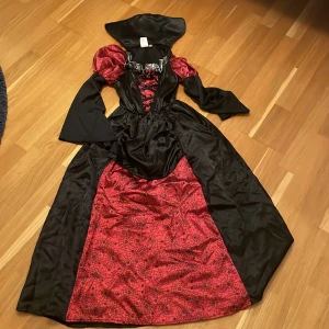 Halloweenklänning - Säljer en cool långklänning i svart och rött med spindelnätsmönster. Klänningen har långa ärmar och en snörning framtill. Perfekt för en halloweenfest eller maskerad! 🕸️