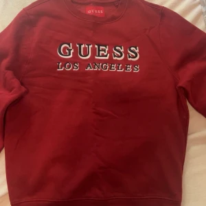 Röd sweatshirt från Guess - Säljer en snygg röd sweatshirt från Guess med texten 'Guess Los Angeles' på framsidan. Tröjan är i storlek M och har en klassisk rund halsringning. Perfekt för en avslappnad stil och passar bra till både jeans och joggers.