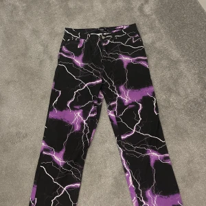 Svarta och lila byxor med blixtmönster från Jaded London - Säljer ett par coola byxor från Jaded London med ett unikt blixtmönster i svart och lila. Byxorna har en skate fit och är perfekta för att sticka ut. De har en knapp och dragkedja framtill. Perfekta för en trendig look! anvädes bara 1 gång då taggen fortfarande sitter kvar kvitto finns via mail vid efterfrågan 