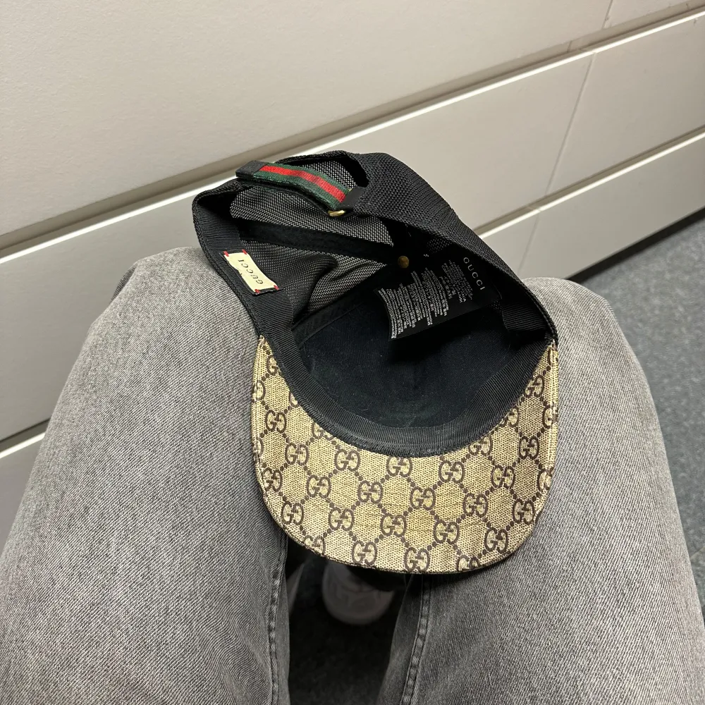 Snygg Gucci keps med det klassiska GG-mönstret i beige och brunt. Baksidan är i svart mesh för bra ventilation och justerbar rem med gröna och röda detaljer. Kepsen är 100% äkta men i använt skick som syns på bilderna därav lägre pris också. Sällsynt och går ej att köpa längre. . Accessoarer.