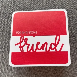 Gratulationskort - Ett gulligt födelsedagskort med pop-up-design. Framsidan har texten 'For an amazing friend' i rött och vitt. Inuti finns färgglada presenter i rött och gult som poppar upp när kortet öppnas. Baksidan har en söt kattillustration i rött.