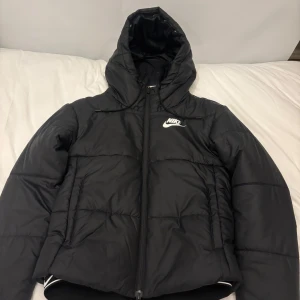 Svart pufferjacka från Nike - Säljer en svart pufferjacka från Nike i storlek XS. Jag har kanske använt den max 2ggr. Jackan har en mysig huva och dragkedja framtill. Perfekt för kalla höst- och vinterdagar. Den är i nyskick och superbekväm att ha på sig. Passar både till vardags och sportiga aktiviteter. 