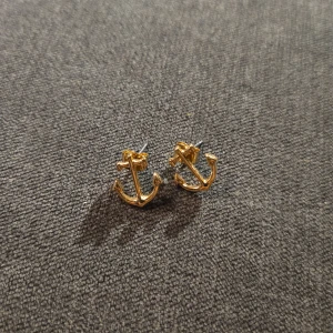 Guldiga ankare örhängen - Säljer ett par snygga guldiga örhängen i form av ankare. Perfekta för att ge en marin touch till din outfit. De är små och diskreta, men ändå stilfulla och passar både till vardags och fest. Köp dem för att lägga till lite glans i din smyckessamling!