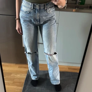 Blå jeans med slitningar - Säljer ett par snygga blå jeans från Gina Tricot i modellen Premium Denim. De är högmidjade och har en straight passform med slitningar på knäna. Storleken är dam S och de är i bra skick.
