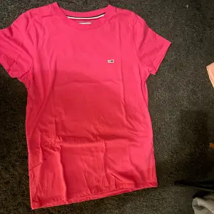 Säljer en snygg rosa t-shirt från Tommy Hilfiger i storlek M. Den är i bomull och har en liten logga på bröstet. Perfekt för sommardagar eller som en casual vardagströja. Skön och stilren design!