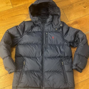 Polo Ralph Lauren dunjacka, marinblå - Säljer min mörkblå och helt oanvända dunjacka från Ralph Lauren.  Jackan är i storlek XL (barn) och  passar dig som är runt 170 cm